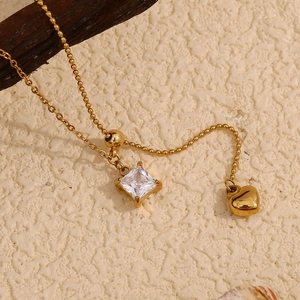 Macro detail of 18K gold plated necklace with square zircon and heart tassel pendant