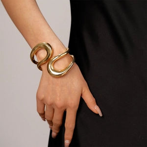 Detailed close-up of a minimalist golden irregular geometric cross cuff bracelet on a wrist