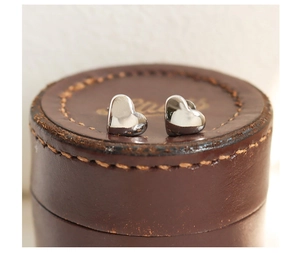 Macro shot of silver heart stud earrings with polished finish on a vintage leather box
