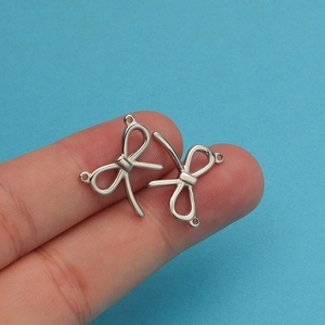 Macro shot of two silver bow-shaped jewelry connectors displayed on a fingertip