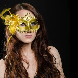 Close-up of golden masquerade mask with feathers and sequins on black background