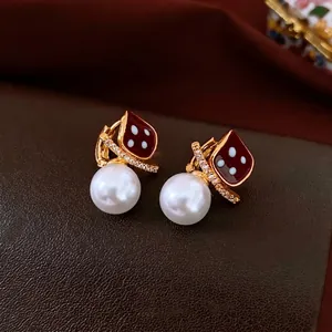 Elegant gold plated square pearl earrings with red diamond pattern on leather background