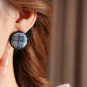 Close-up of a model wearing navy blue plaid fabric earrings with a black round border
