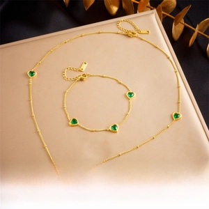 Detail of gold bead chain jewelry set with green heart-shaped gemstones and lobster clasp