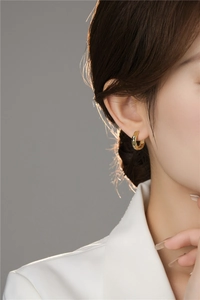 Detailed close-up of a model wearing a gold geometric faceted hoop earring with texture