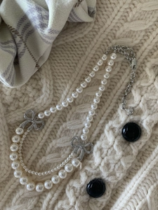Détail d'un collier de perles multicouche avec nœuds argentés sur un pull en maille beige