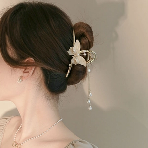 Detail view of a gold flower hair claw with pearl butterfly design and long tassels