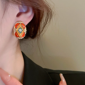 Close-up of vintage orange enamel earrings with gold edges and pearl detail on ear