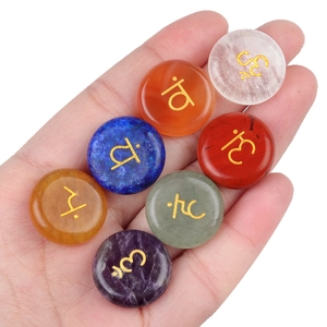 Set of seven natural chakra stones with gold yoga symbols held against white background
