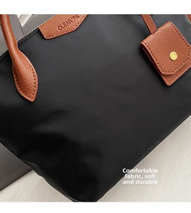 Detail of black nylon tote featuring brown lychee grain leather trim and clear logo emboss