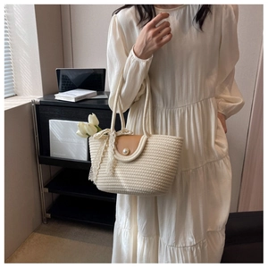 Detail of beige straw tote with brown leather flap and pearl clasp on a rope handle