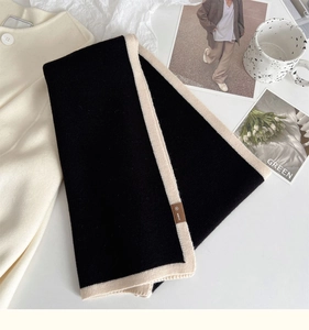Detail of black and beige knit scarf featuring fine texture and leather logo patch