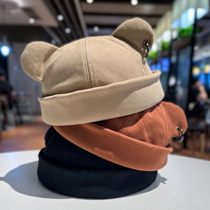 Three knitted beanie hats with bear ears in khaki, red, and black with metal ring detail