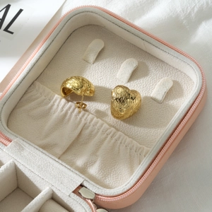 Macro view of gold hammered heart earrings inside a pink leather jewelry storage box