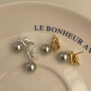 Detailed close-up of grey pearl knot earrings in gold and silver finishes on a tray