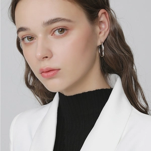Close-up of silver twisted hoop earrings worn by a model in a white blazer