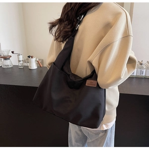 Detail view of large black canvas hobo bag with fashion logo on shoulder of a model
