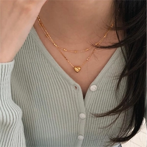 Close-up of double-layered gold heart necklace showing polished puffed pendant detail