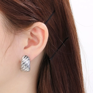 Vue macro de boucles d'oreilles créoles C argentées avec texture spirale striée