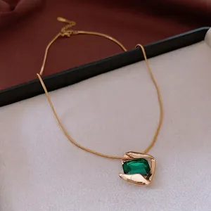 Golden snake chain necklace with emerald green gemstone and fluid geometric pendant