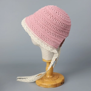 Detail of baby pink knit bonnet featuring delicate off-white lace trim and long ribbon ties