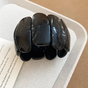 Detailed close-up of a wide acrylic bracelet featuring black marble patterns on a white tray