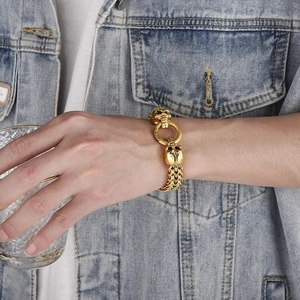 Detail of a men's gold punk skull bracelet worn by a model holding a glass cup