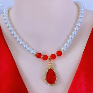 Elegant white pearl necklace with a red teardrop gemstone pendant on a gold metal frame