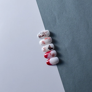 Macro detail of white press-on nails with red spider lily and black butterfly motifs