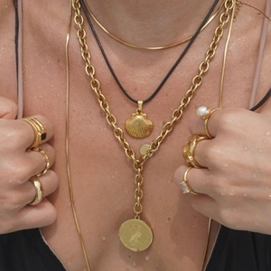 Close-up of golden multi-layered necklaces with shell and coin pendants on wet skin