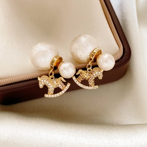 Detailed macro view of gold pony earrings with zircons and pearls on white silk