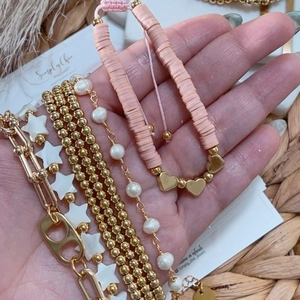 Detail of layered gold-plated beaded bracelets with star charms, pearls, and pink clay discs