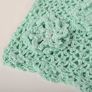Macro detail of mint green hand-crocheted hollow texture with 3D flower and pearl