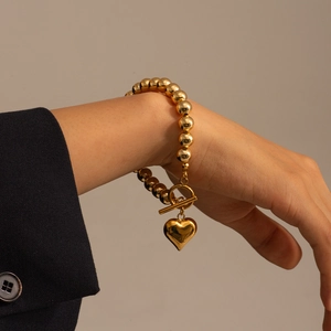 Detail of a gold beaded bracelet with a polished heart pendant and a stylish T-bar closure