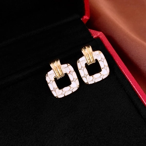 Detail of square gold earrings with white enamel and sparkling zircon on black velvet