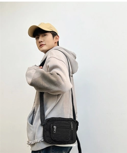 Detail shot of mini black denim crossbody bag with adjustable strap on grey sweatshirt