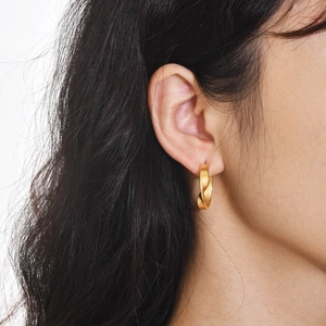 Close-up of gold-plated twisted hoop earring worn by model showing texture and size