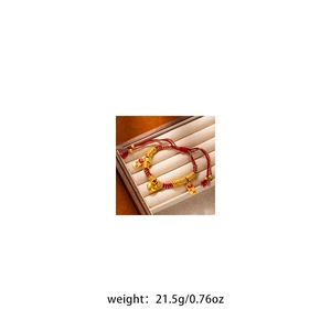 Detail of red and blue braided bracelet with golden beads and Ping An charm on velvet