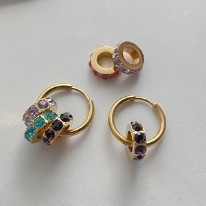 Detailansicht von goldenen Edelstahl-Creolen mit bunten Zirkon-Anhängern