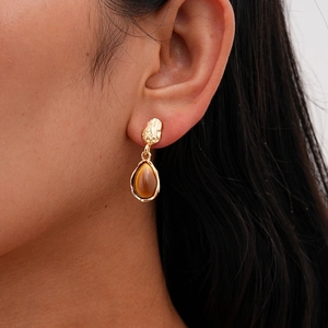Close-up of golden irregular textured earrings with brown teardrop resin gemstone