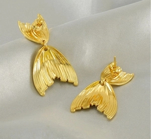 Detailed macro view of 18K gold plated fishtail stud earrings on silver silk fabric