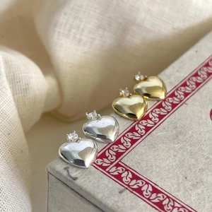 Detail view of heart-shaped silver and gold stud earrings with cubic zirconia stones