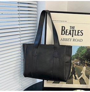 Detail shot of black leather tote bag with decorative stitching against a retro backdrop