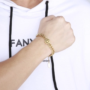 Detail of a gold Cuban link chain bracelet featuring a signature smiley face charm on wrist