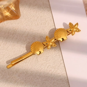 Detail view of 18K gold plated seashell and starfish hair clips on a beige textured surface