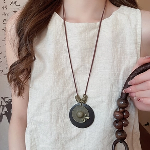 Close-up of vintage pendant necklace featuring a wood round base and metal hat charm detail