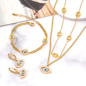 Golden Evil Eye jewelry set with layered necklace, bracelet, and earrings on marble