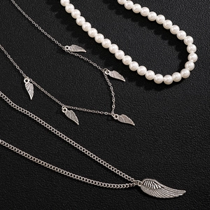 Men's silver wing pendant necklace set with white pearls on a textured black background