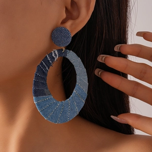 Detail of oversized oval denim earrings featuring blue fabric patchwork and white stitching