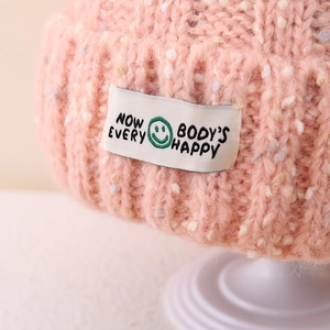 Detail of pink knit beanie featuring colorful dots and a happy face woven label